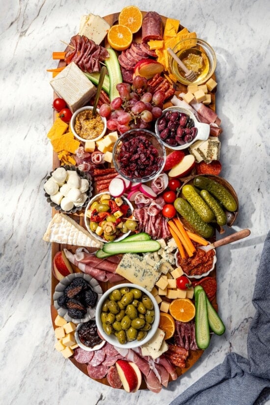 Your ultimate guide to creating a charcuterie and cheese board! I'll show you how to choose and arrange everything for a beautiful spread. Charcuterie board in process, with cheese, meats, pickles, and more.