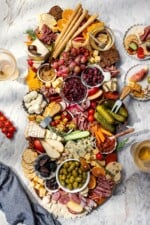 Plates surrounding large charcuterie and cheese board with fruit, pickles, olives, and spreads.