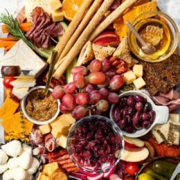 Charcuterie and cheese board with fruit, olives, and spreads.