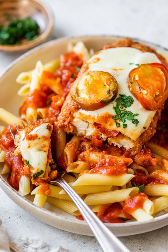 Spicy Vodka Chicken Parmesan is made with hot cherry peppers, vodka sauce, fresh mozzarella, and breaded chicken cutlets. Baked or air fryer! Spicy Vodka Chicken Parmesan on a plate over pasta