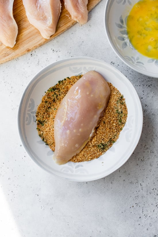 Spicy Vodka Chicken Parmesan is made with hot cherry peppers, vodka sauce, fresh mozzarella, and breaded chicken cutlets. Baked or air fryer! A chicken breast in a bowl of breading