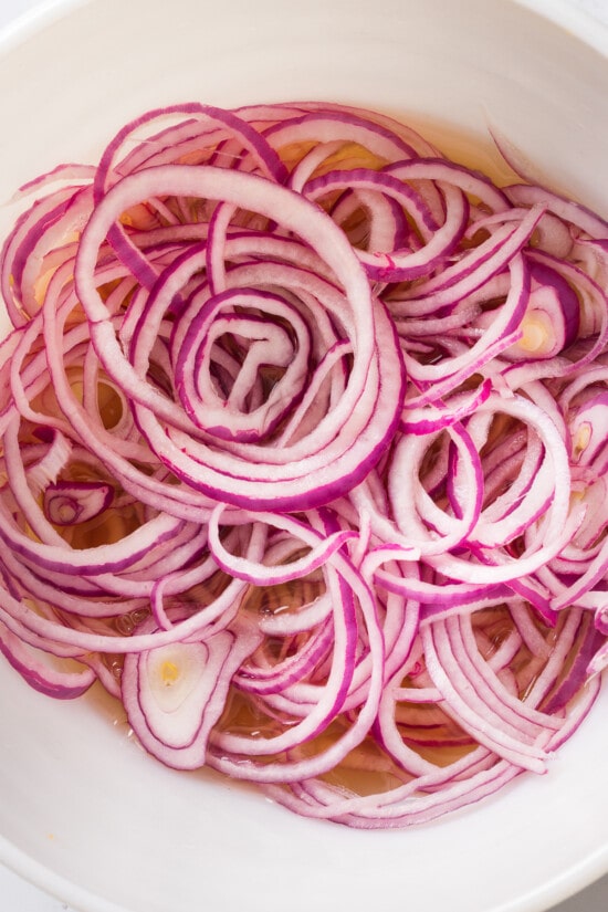 These easy pickled red onions are add a tangy, slightly sweet, and crunchy element to steaks, sandwiches, tacos, burrito bowls and more! sliced red onions