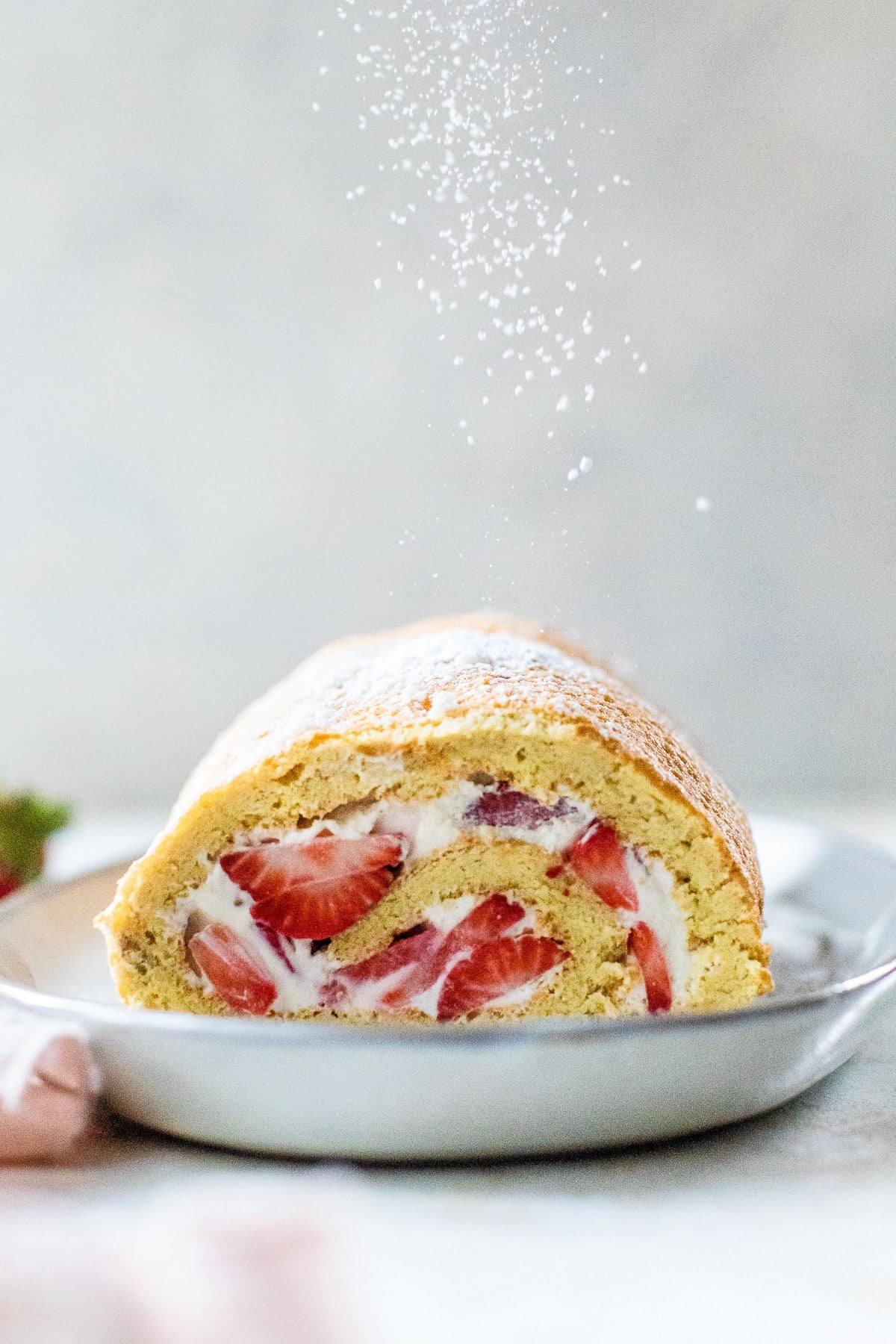 This Strawberry Swiss Roll features a soft sponge cake, sweet cream, and fresh strawberries. So simple & perfect when berries are in season. Strawberry Swiss Roll on a plate, sliced in half.