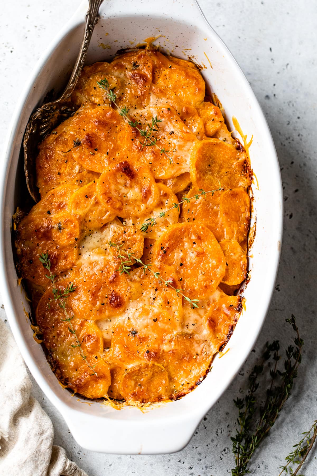 Make sweet potatoes au gratin inspired by Pommes Anna, a French dish of creamy, thinly sliced potatoes topped with melted Gruyere cheese. Overhead view of sweet potato gratin in an oval casserole dish.