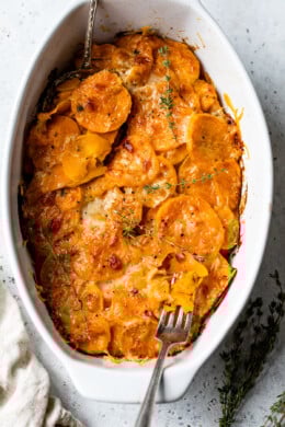 Overhead view of a fork resting in a casserole dish of sweet potatoes au gratin.
