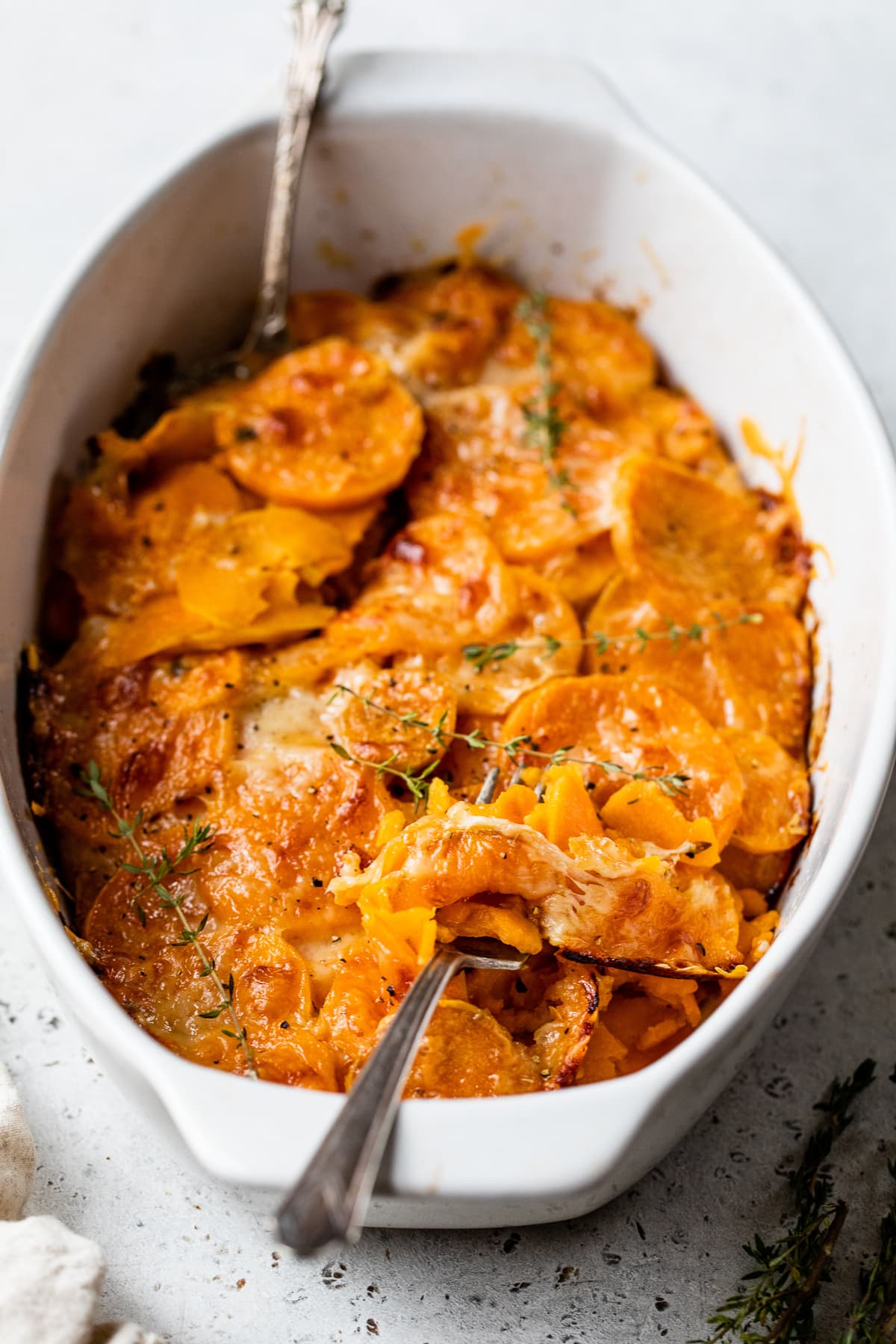 Make sweet potatoes au gratin inspired by Pommes Anna, a French dish of creamy, thinly sliced potatoes topped with melted Gruyere cheese. Sweet potato gratin served in an oval casserole dish.