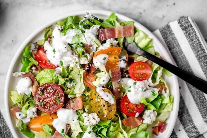 Classic wedge salad meets chopped salad in this easy side salad dish made with lettuce, bacon, tomatoes, blue cheese and chives with a light homemade blue cheese dressing.