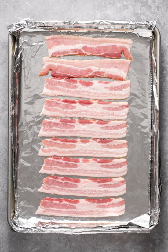 Whether you're a fan of tender, crisp, or extra crispy bacon, this simple method of cooking bacon in the oven is easy. No stovetop mess! Raw bacon on a foil lined baking sheet.