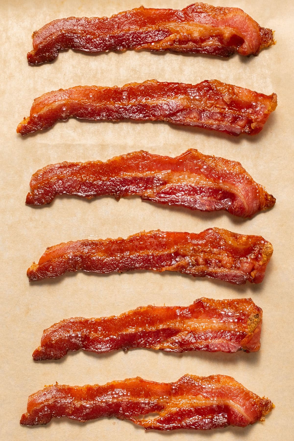 Whether you're a fan of tender, crisp, or extra crispy bacon, this simple method of cooking bacon in the oven is easy. No stovetop mess! Bacon on parchment paper.