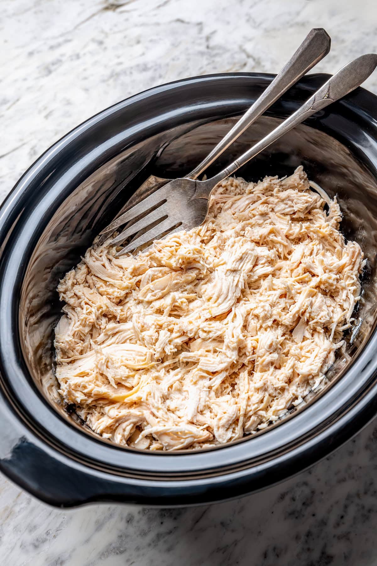Shredded chicken in slow cooker with forks