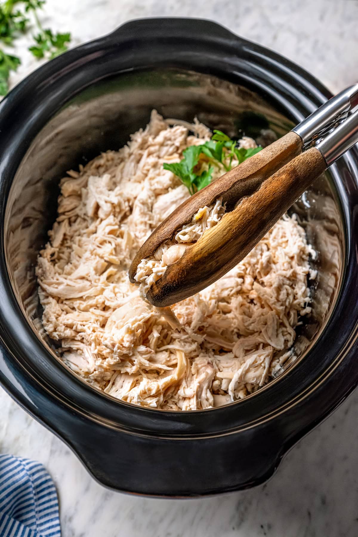 This slow cooker shredded chicken recipe is juicy, tender, and flavorful. It's a hands-off cooking method perfect for meal prep! Tongs grabbing shredded chicken from slow cooker