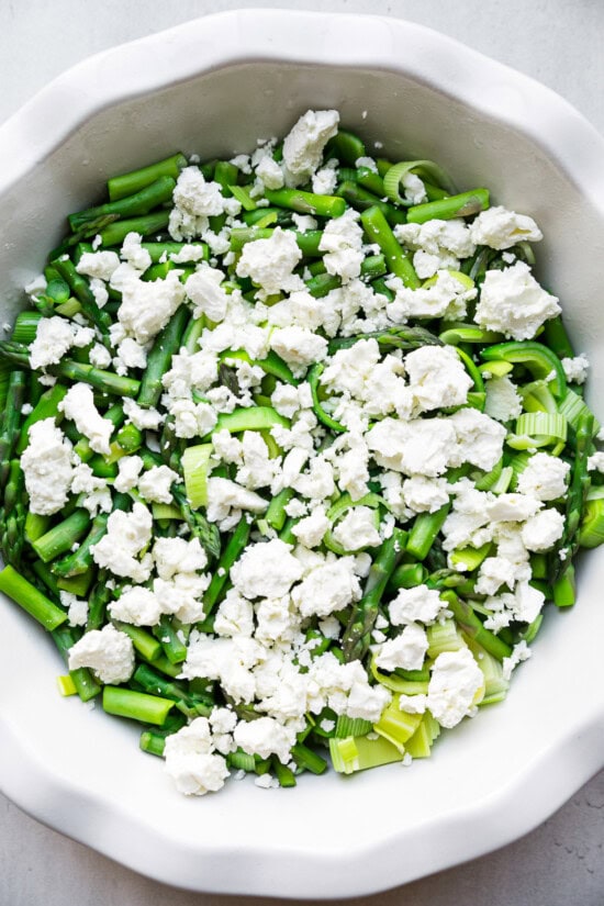 Add veggies and feta to a quiche dish.