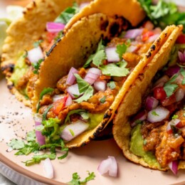 Plate with 3 lentil tacos topped with cilantro and red onion