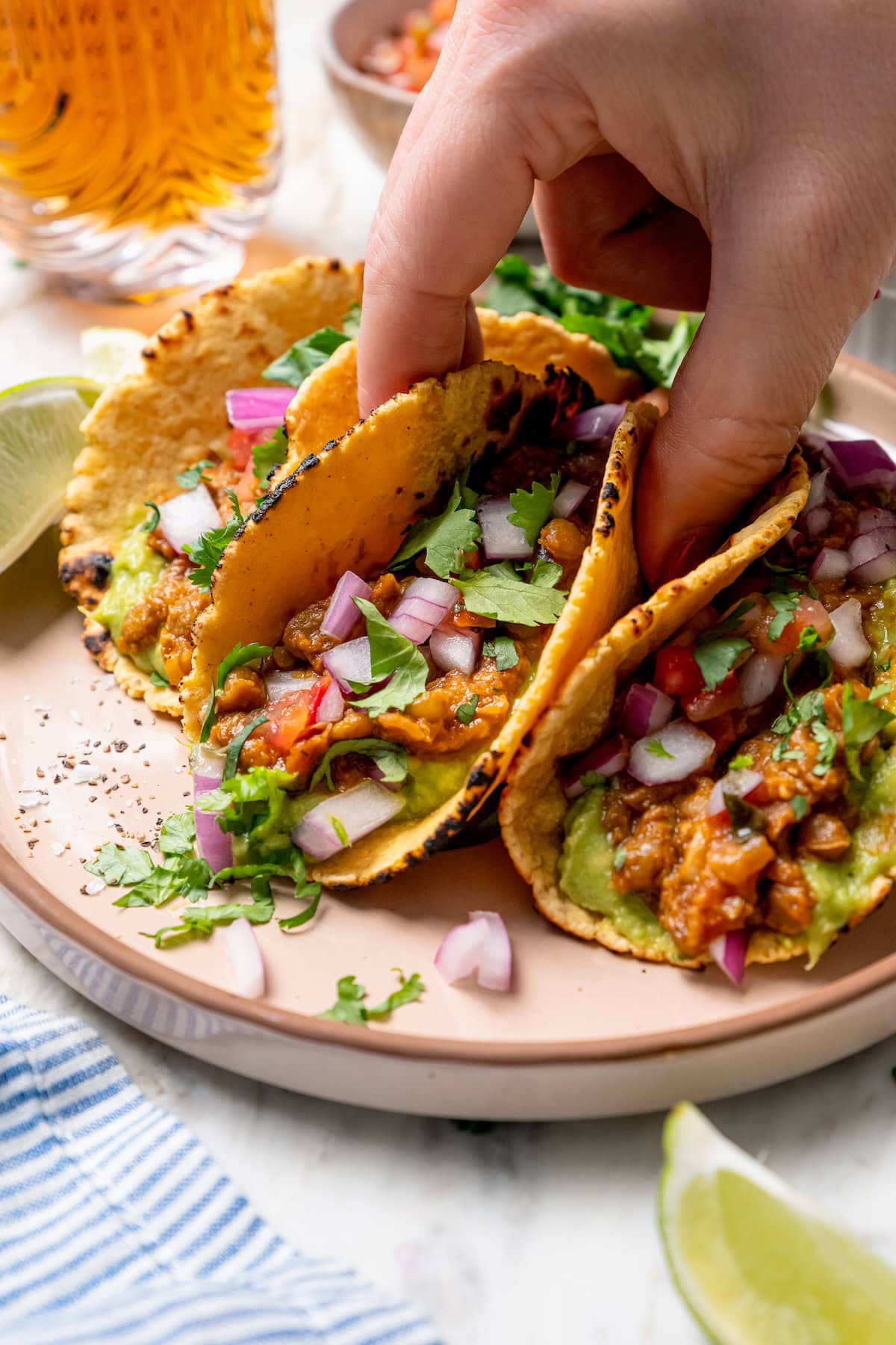 These vegan lentil tacos are easy to make, full of big Tex-Mex flavor and great for meal prep. Add your favorite toppings and dig in! Hand lifting lentil taco from plate