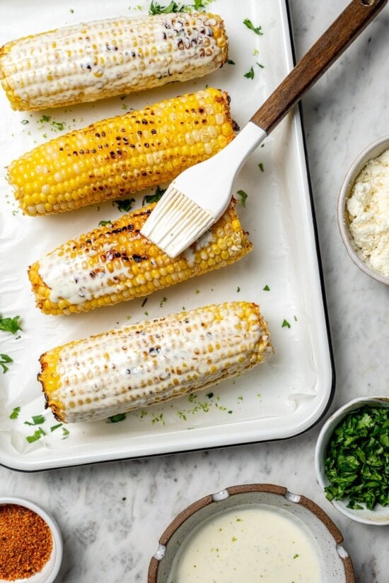 This lighter version of the classic grilled Mexican street corn recipe has all the flavor of the original, with mayo, cotija, lime and Tajín! Brushing grilled corn with lime mayo mixture