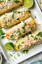 Overhead view of 4 ears of Mexican street corn in pan with cilantro and lime
