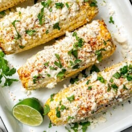 Overhead view of 4 ears of Mexican street corn in pan with cilantro and lime