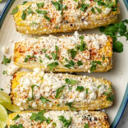 Overhead view of 4 ears of Mexican street corn on platter with cilantro and lime wedges