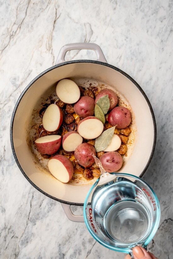 With spicy chorizo, potatoes, corn, crab, clams and shrimp, this seafood boil recipe is a complete meal in one pot. So easy to make too! Pouring water into Dutch oven with bay leaves and potatoes