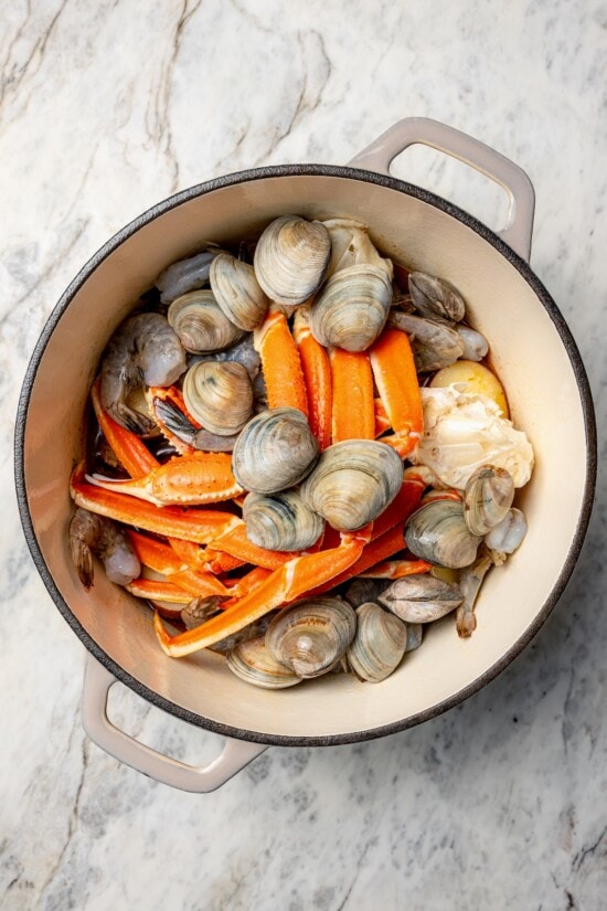 With spicy chorizo, potatoes, corn, crab, clams and shrimp, this seafood boil recipe is a complete meal in one pot. So easy to make too! Overhead view of clams, shrimp, and crab legs added to Dutch oven
