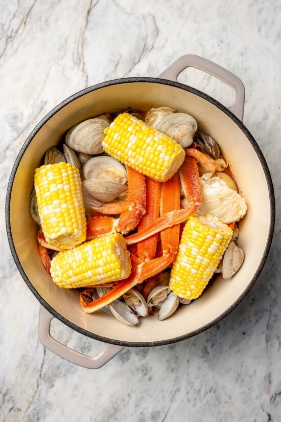 With spicy chorizo, potatoes, corn, crab, clams and shrimp, this seafood boil recipe is a complete meal in one pot. So easy to make too! Overhead view of corn added to pot of seafood