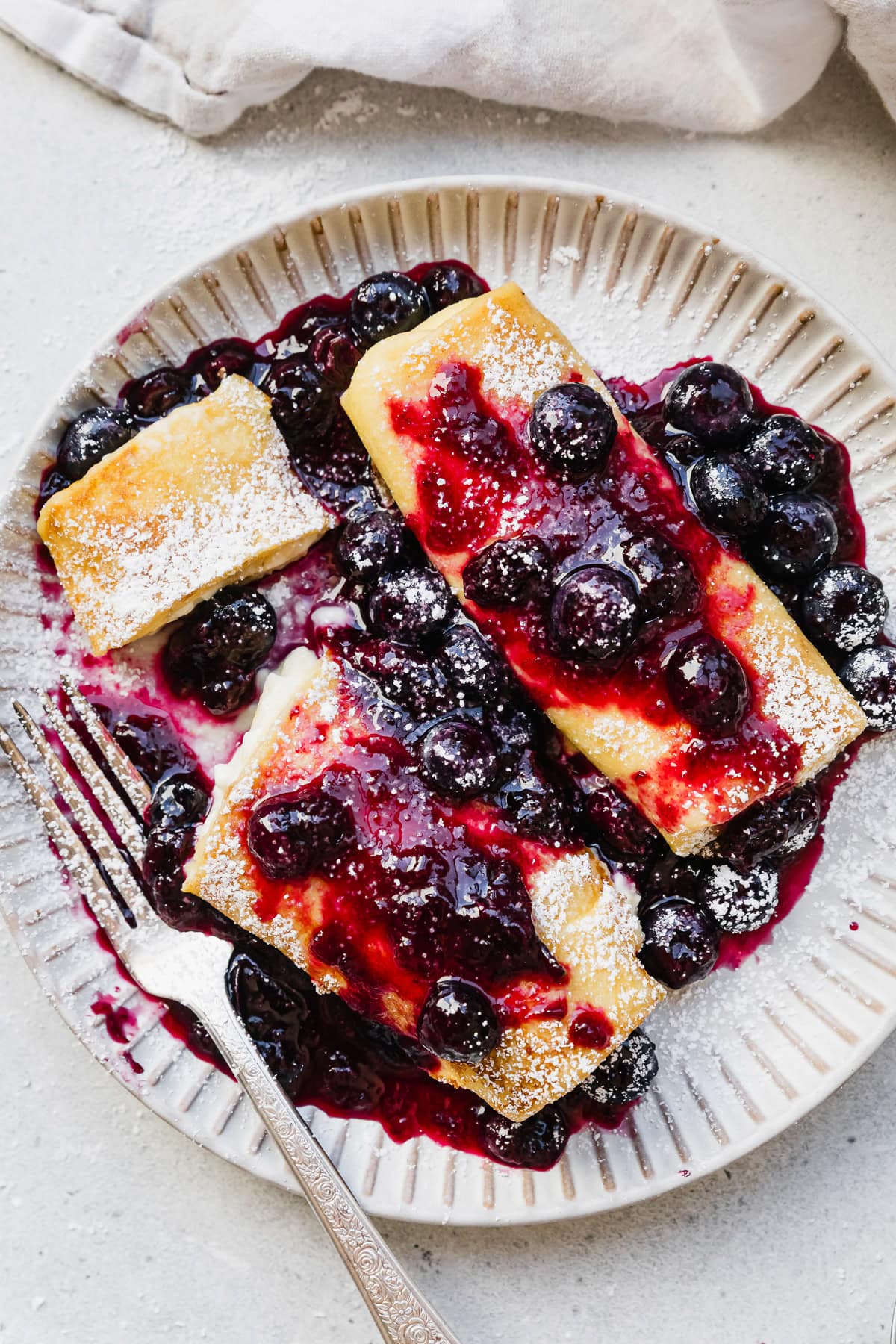 Cooked cheese blintzes on plate with blueberry sauce