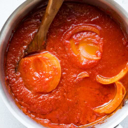 Lightened Marcella Hazan-inspired tomato sauce simmering in a pot with a halved onion