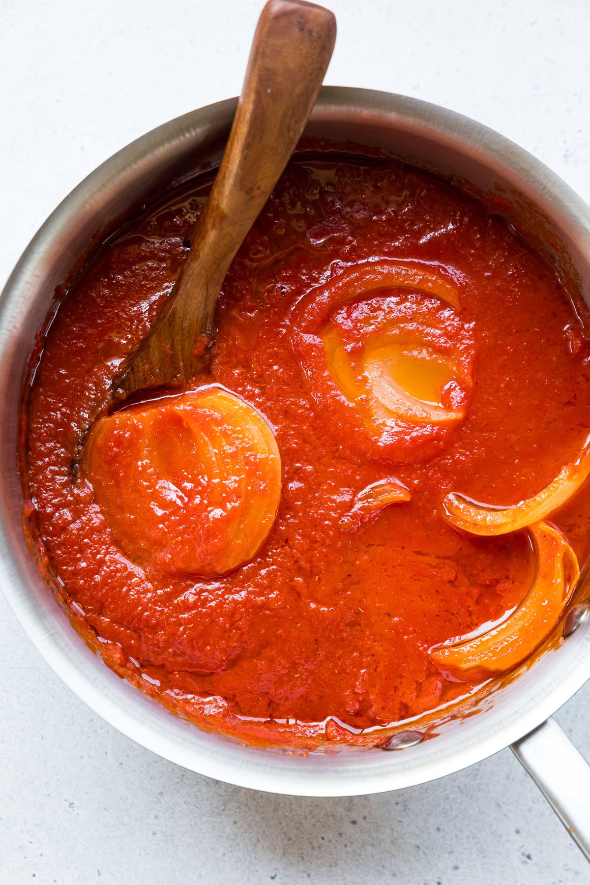 Lightened Marcella Hazan-inspired tomato sauce simmering in a pot with a halved onion