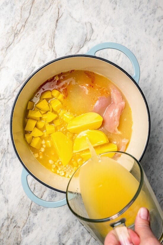 Pouring broth into dutch oven for chicken corn chowder.