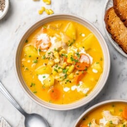 Two bowls of creamy chicken corn chowder on marble tabletop.