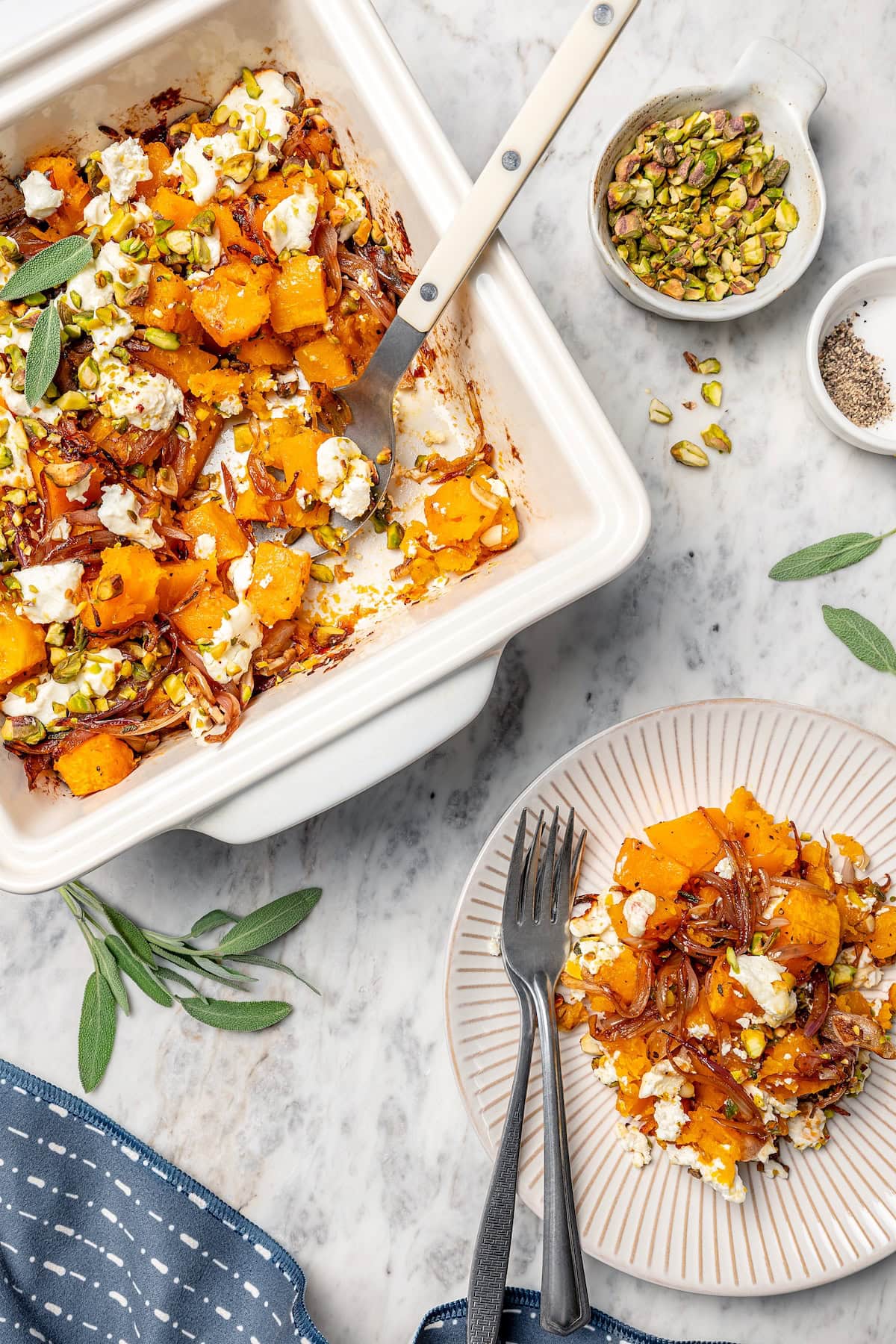 Baked butternut squash is layered with creamy goat cheese, shallots, and pistachios in this cozy side dish recipe. Perfect for the holidays! Butternut squash bake in pan and on plate.