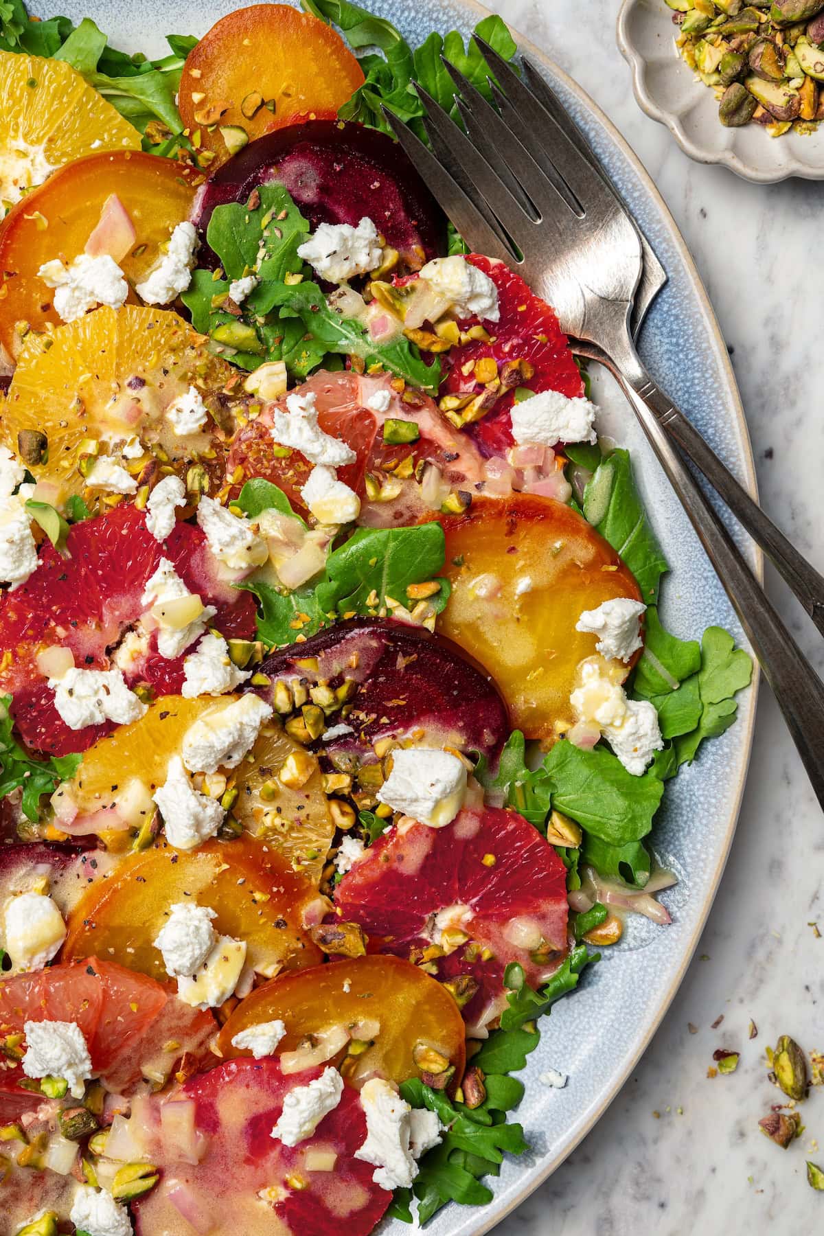 This Roasted Beet and Citrus Salad pairs tender beets with creamy goat cheese, citrus fruit and pistachios for a show-stopping holiday side! Roasted beet and citrus salad on platter with two forks.