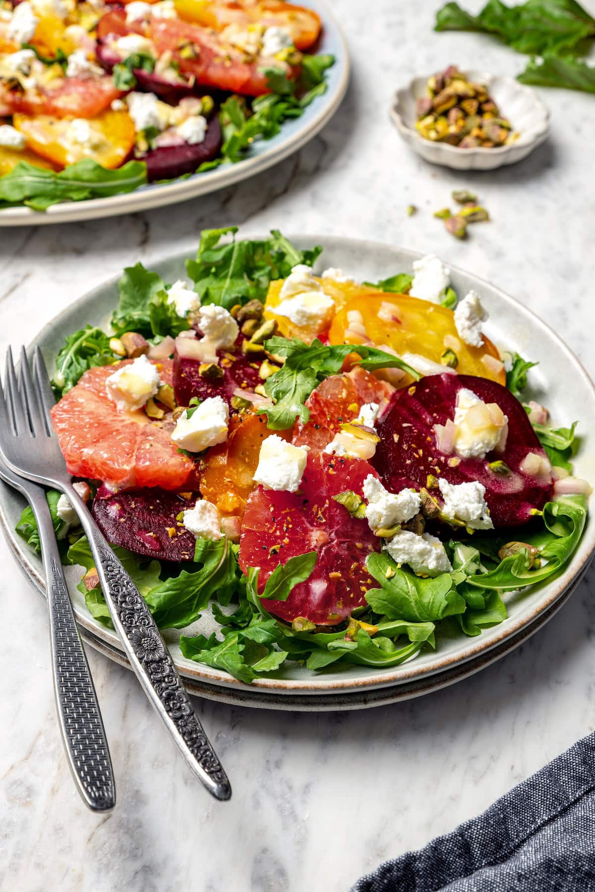 This Roasted Beet and Citrus Salad pairs tender beets with creamy goat cheese, citrus fruit and pistachios for a show-stopping holiday side! Roasted beet and citrus salad on plate with two forks.
