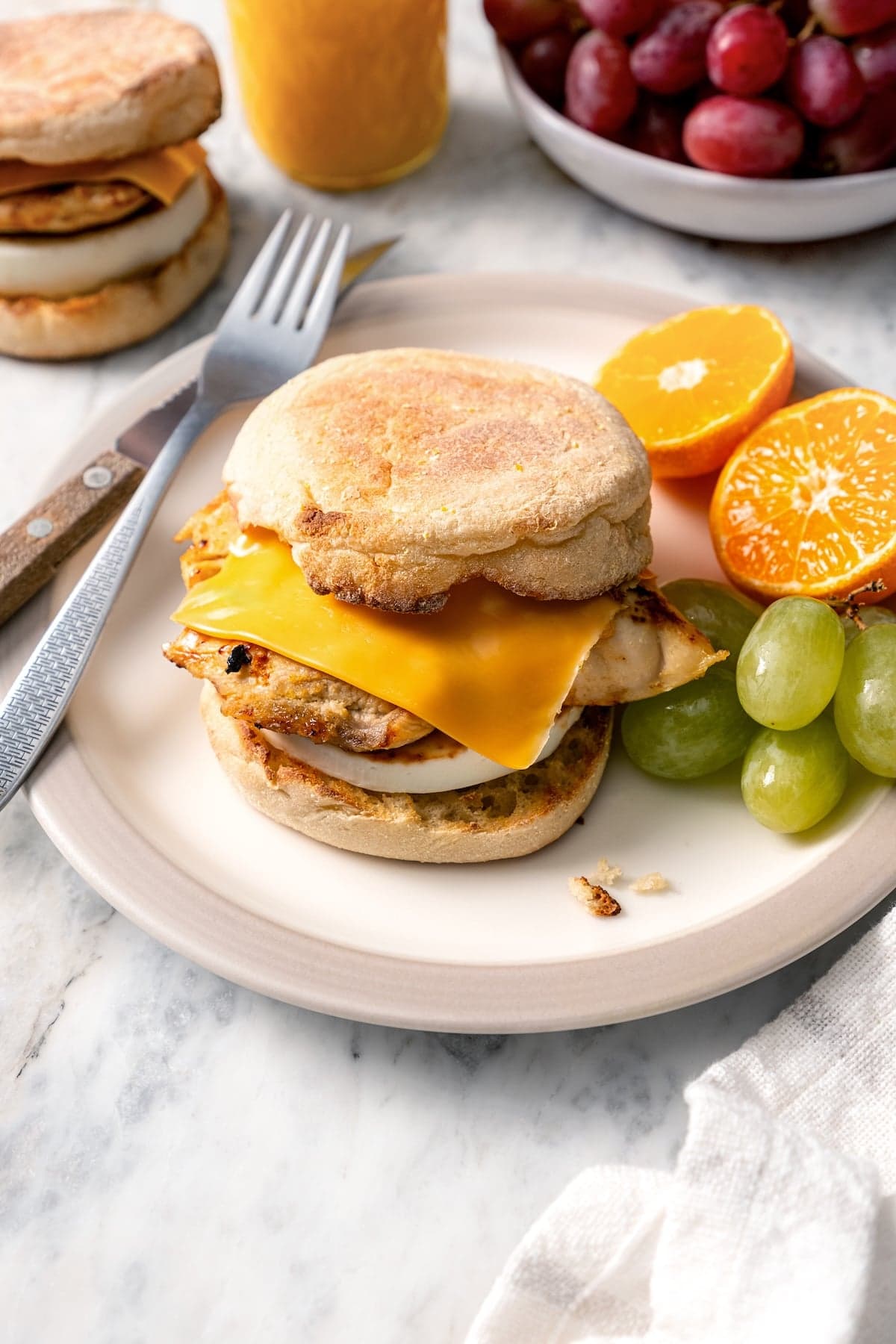 This Chick-Fil-A Egg White Grill copycat is made with juicy grilled chicken, fluffy egg whites and cheese for a hearty meal prep breakfast! Copycat Chick-fil-A egg white grill sandwich on plate with grapes and orange halves.