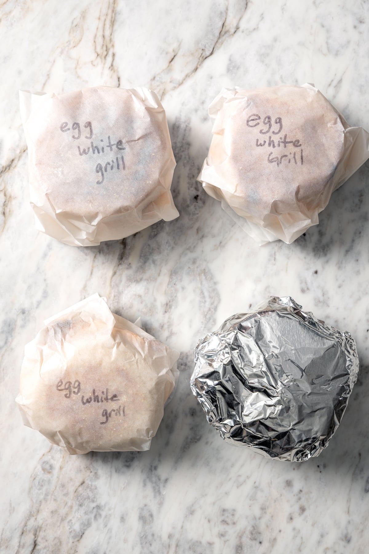 This Chick-Fil-A Egg White Grill copycat is made with juicy grilled chicken, fluffy egg whites and cheese for a hearty meal prep breakfast! 3 egg white grill sandwiches wrapped in parchment paper and one wrapped in foil.